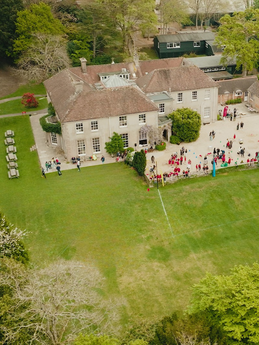 Aerial view of the stone school building and surrounding green grounds.