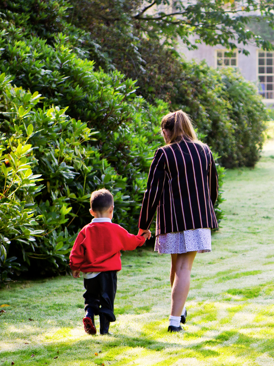 An older student and a young child holding hands while walking through the school gardens.