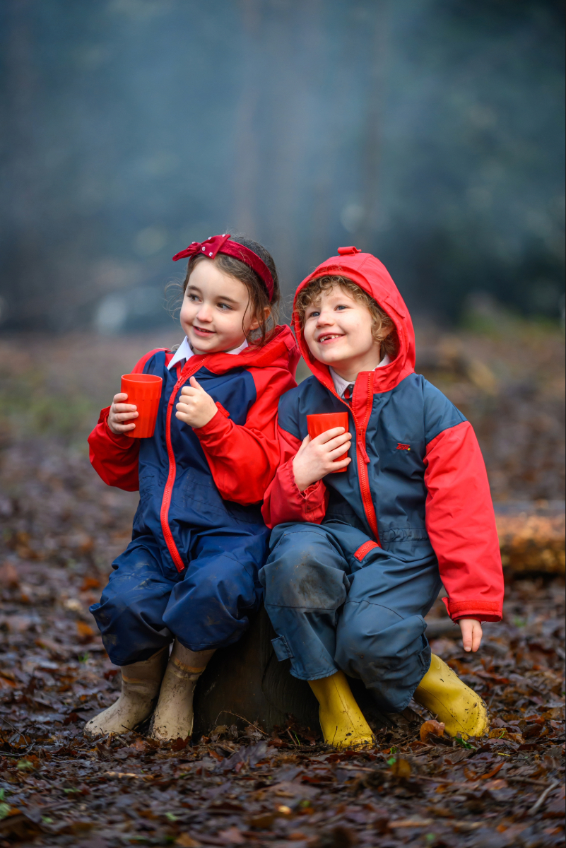 two students sitting on a tree trunk holding red cups in the woodland