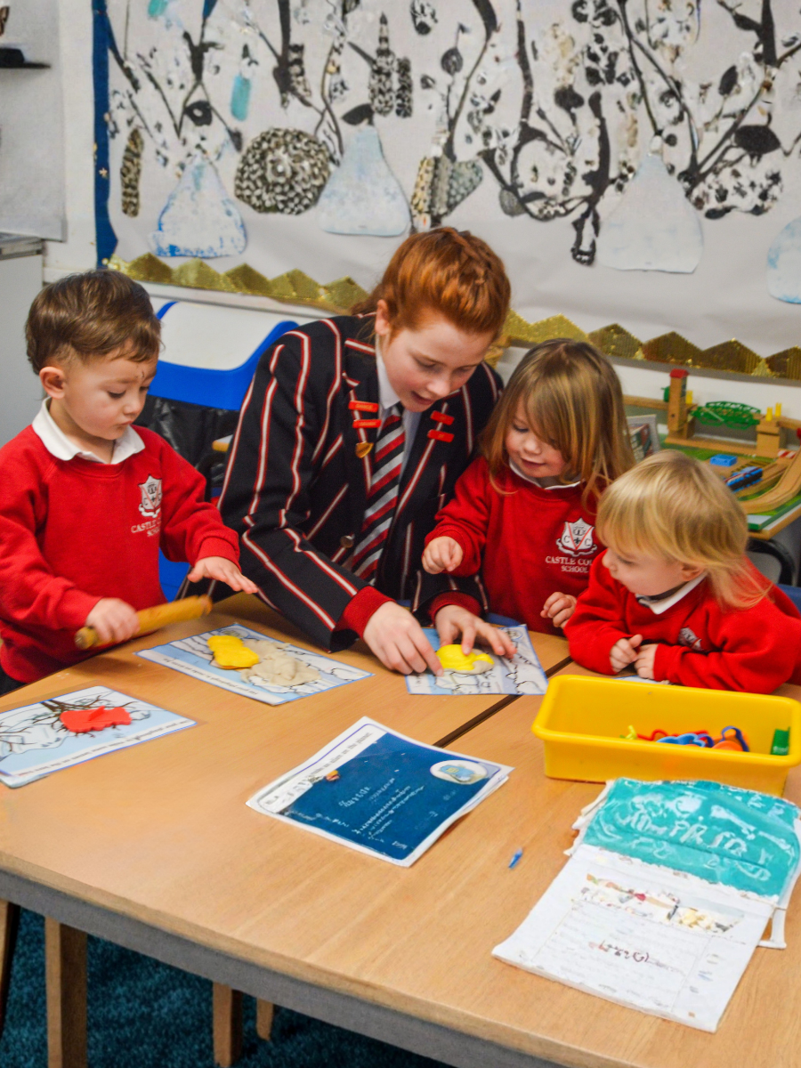 A senior student helping nursery children with a playdough activity in a classroom.
