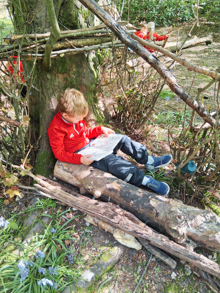 photo of a student sat by a tree reading a book