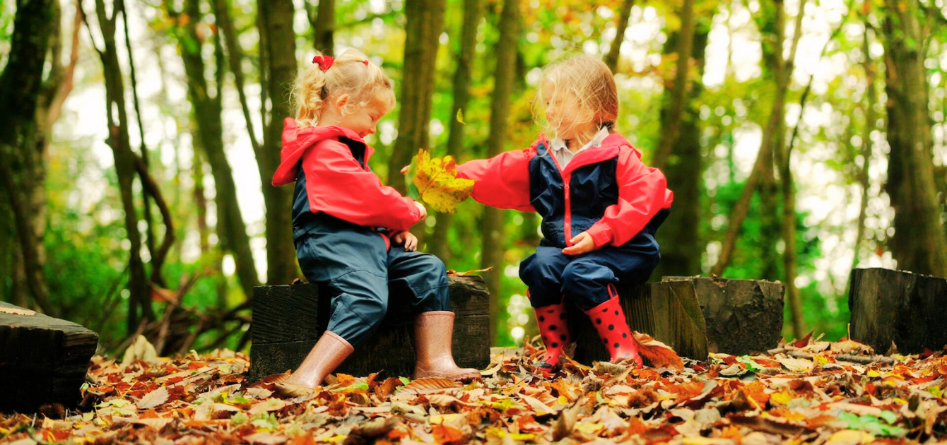 two girls playing with autumn leaves in the woodland
