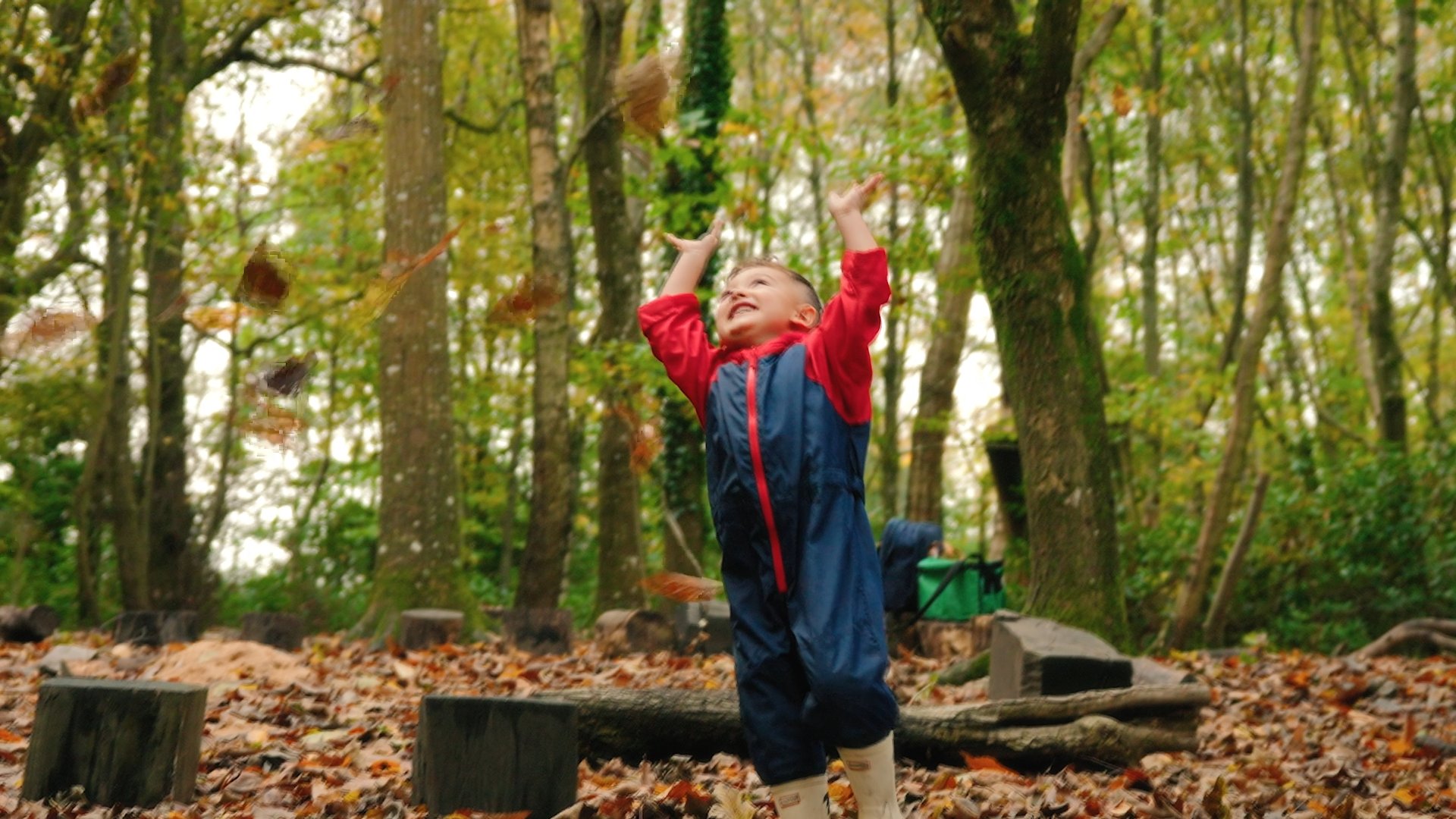 photo of nursery student playing in the autumn leaves in the woodland